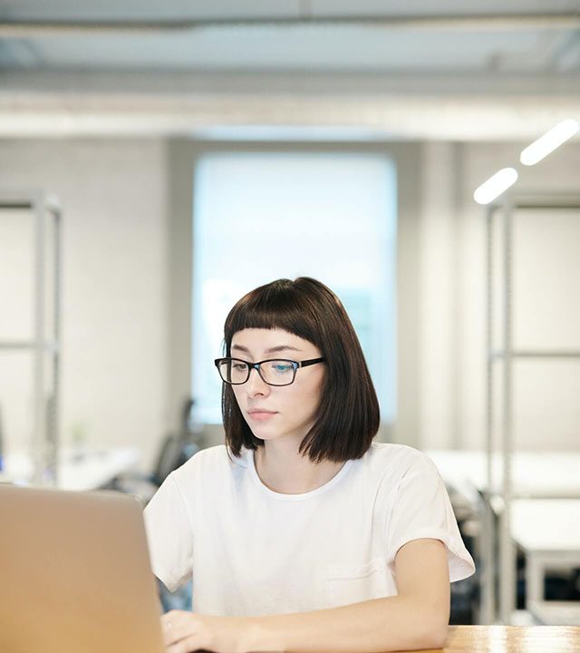 Young woman wearing glasses working on a laptop in an office.